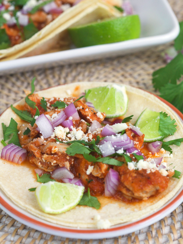 A chicken tinga taco is presented with lime wedges.