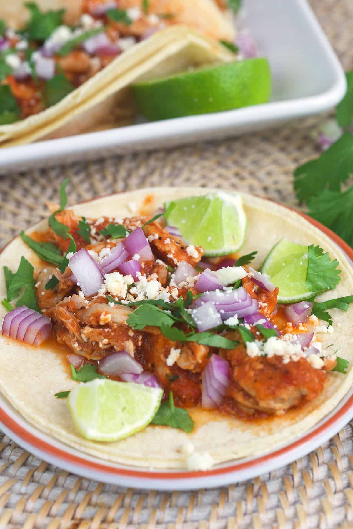 A chicken tinga taco is presented with lime wedges.