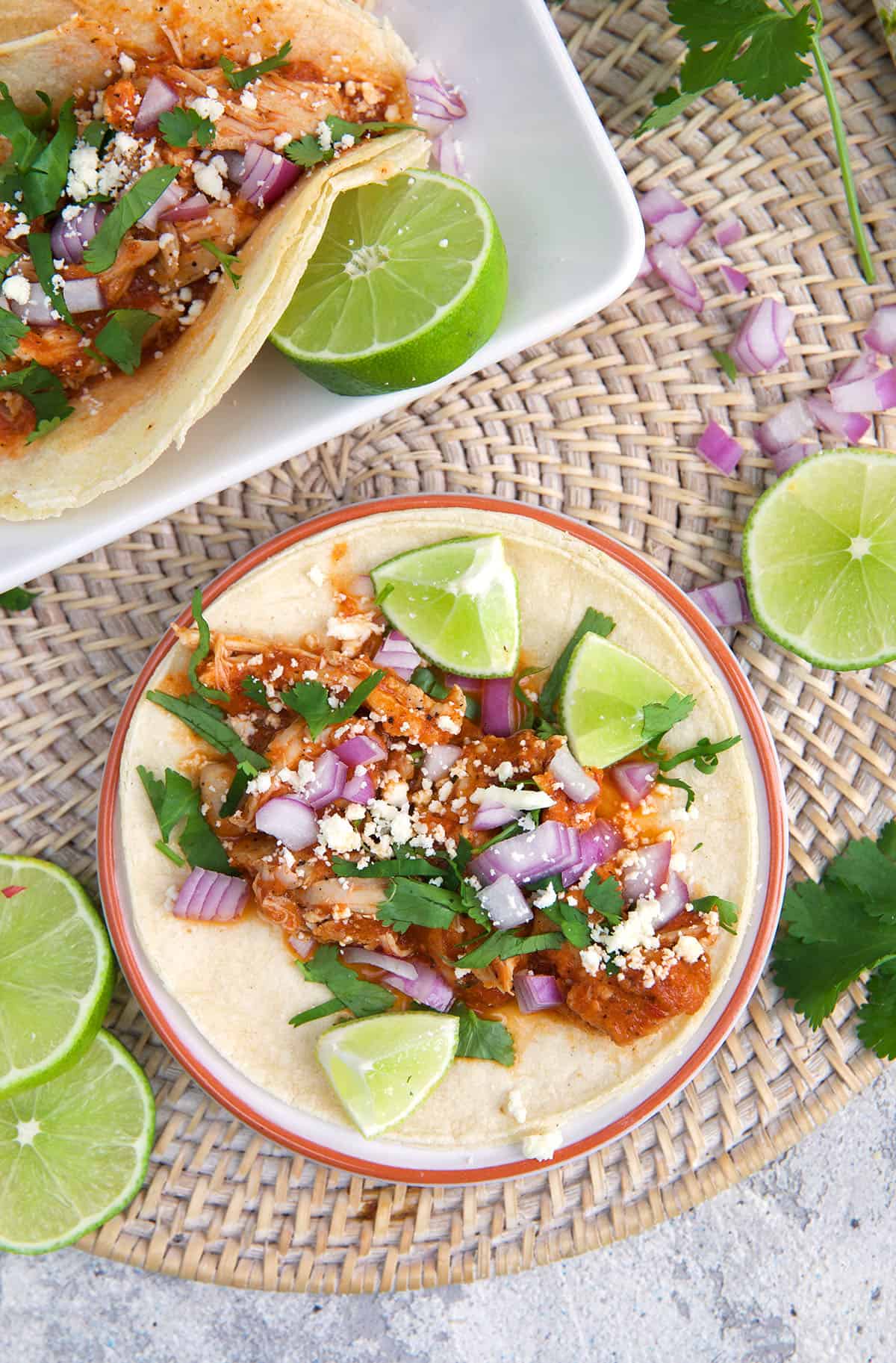 Tacos are garnished with cilantro, cheese, onions and limes.