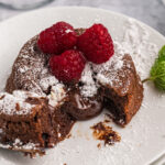 Fresh raspberries and powdered sugar are placed on top of a chocolate lava cake.