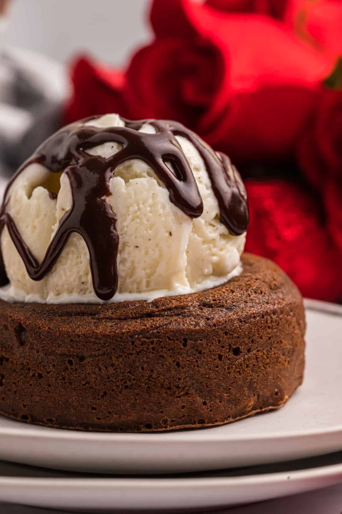 A scoop of vanilla ice cream drizzled with chooclate sauce is on top of a molten lava cake.