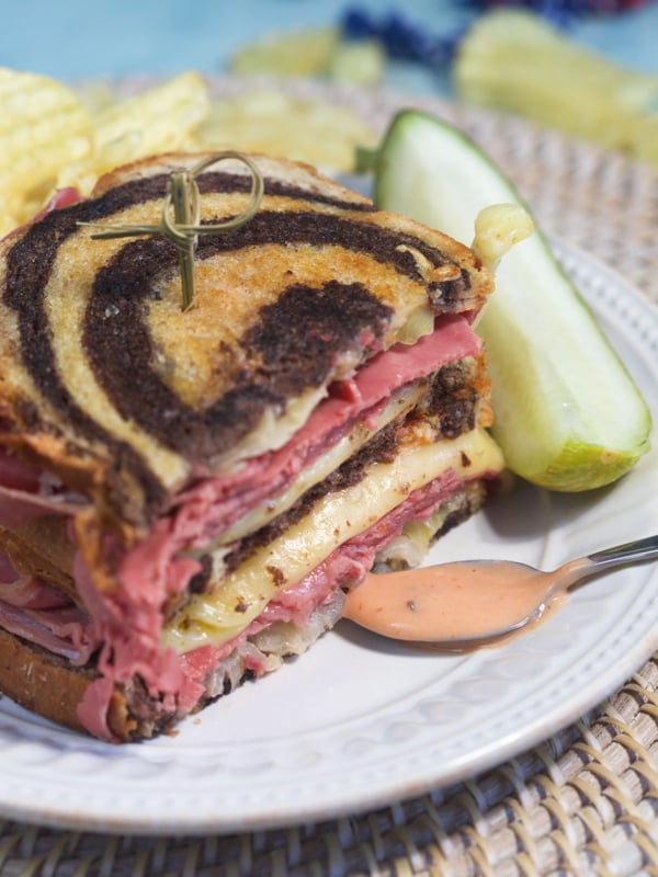 A spoon with orange dressing on it is placed next to a halved sandwich.