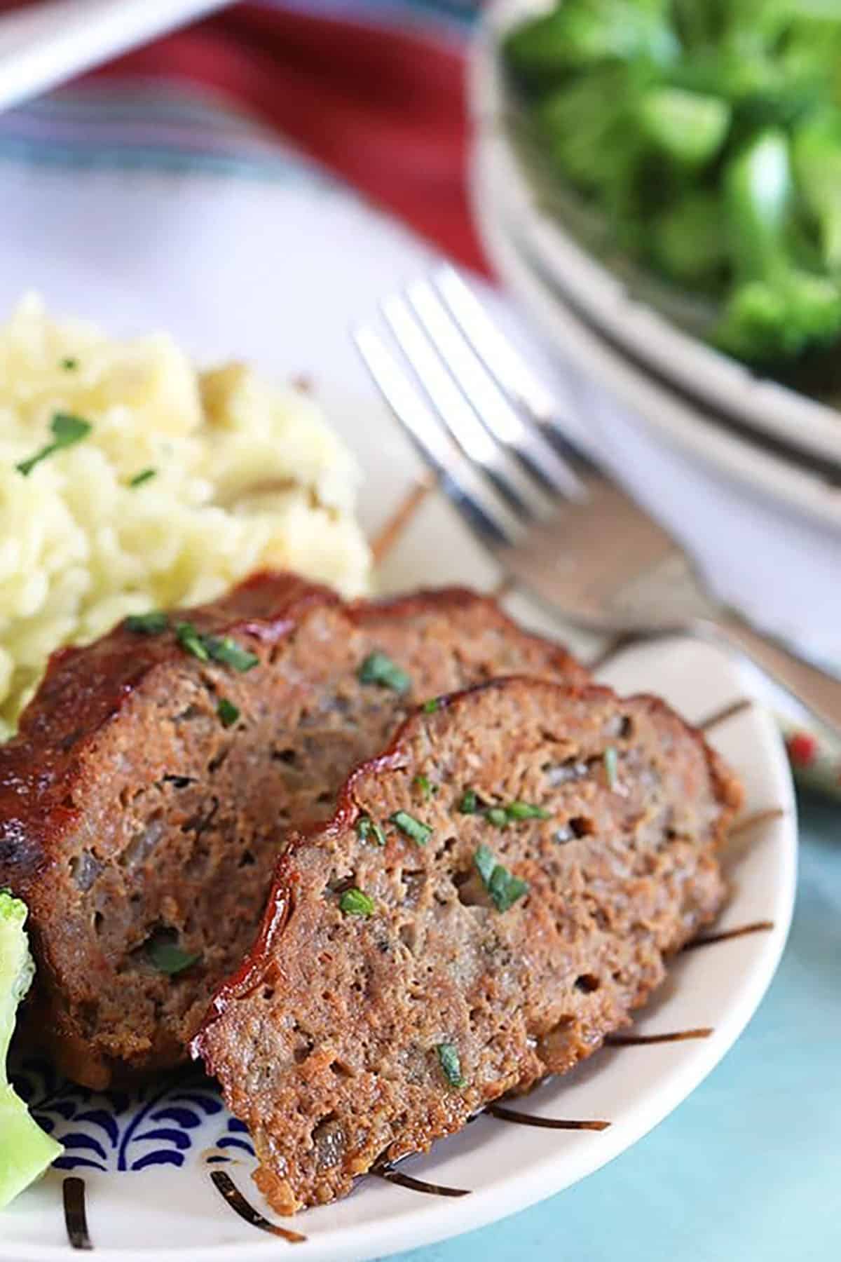 Two slices of crockpot meatloaf on a white plate with mashed potatoes.