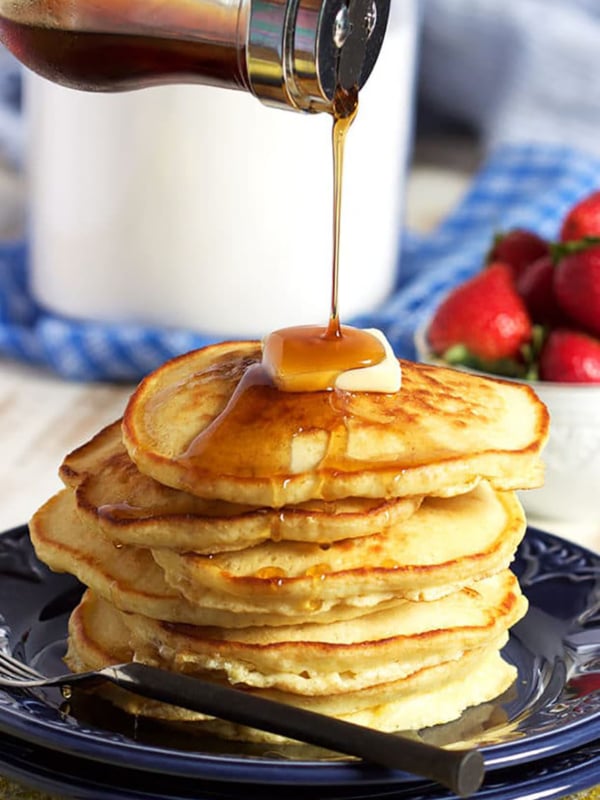 Stack of pancakes with a pat of butter on top and syrup being poured over top.