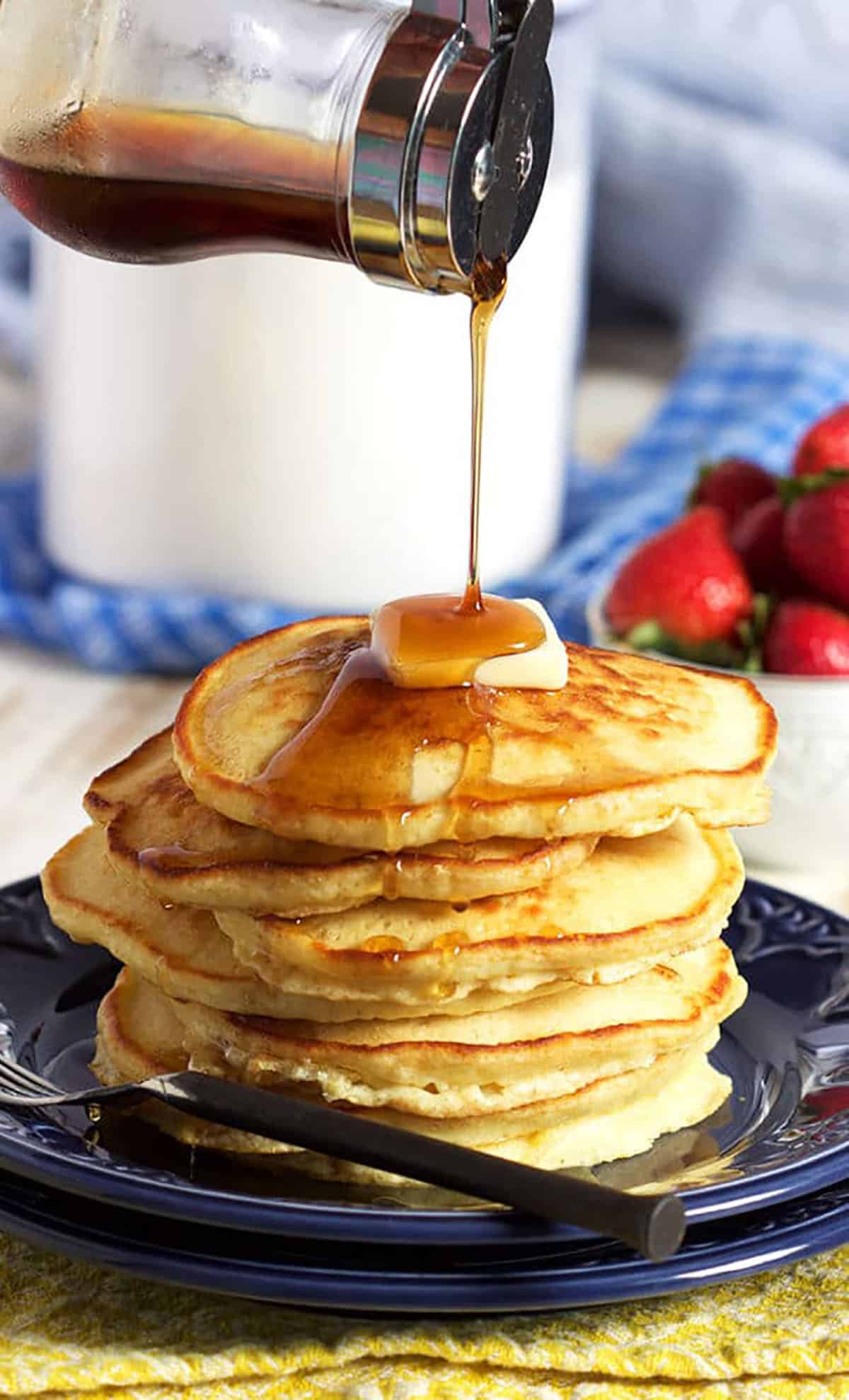 Stack of pancakes with a pat of butter on top and syrup being poured over top.