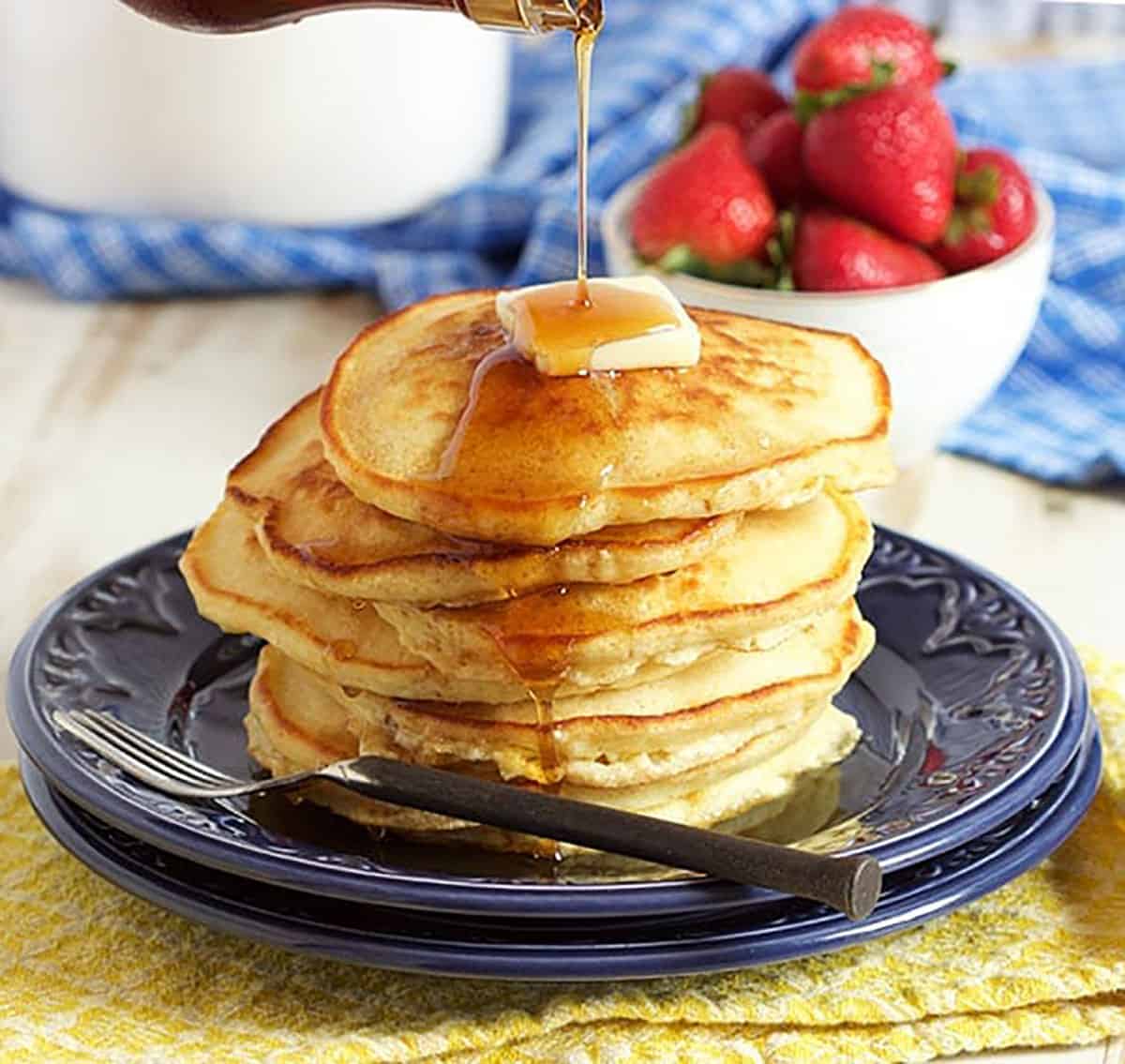 Stack of pancakes on a blue plate with a pat of butter and syrup on top