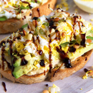 Two slices of avocado hummus toast are drizzled with balsamic glaze.