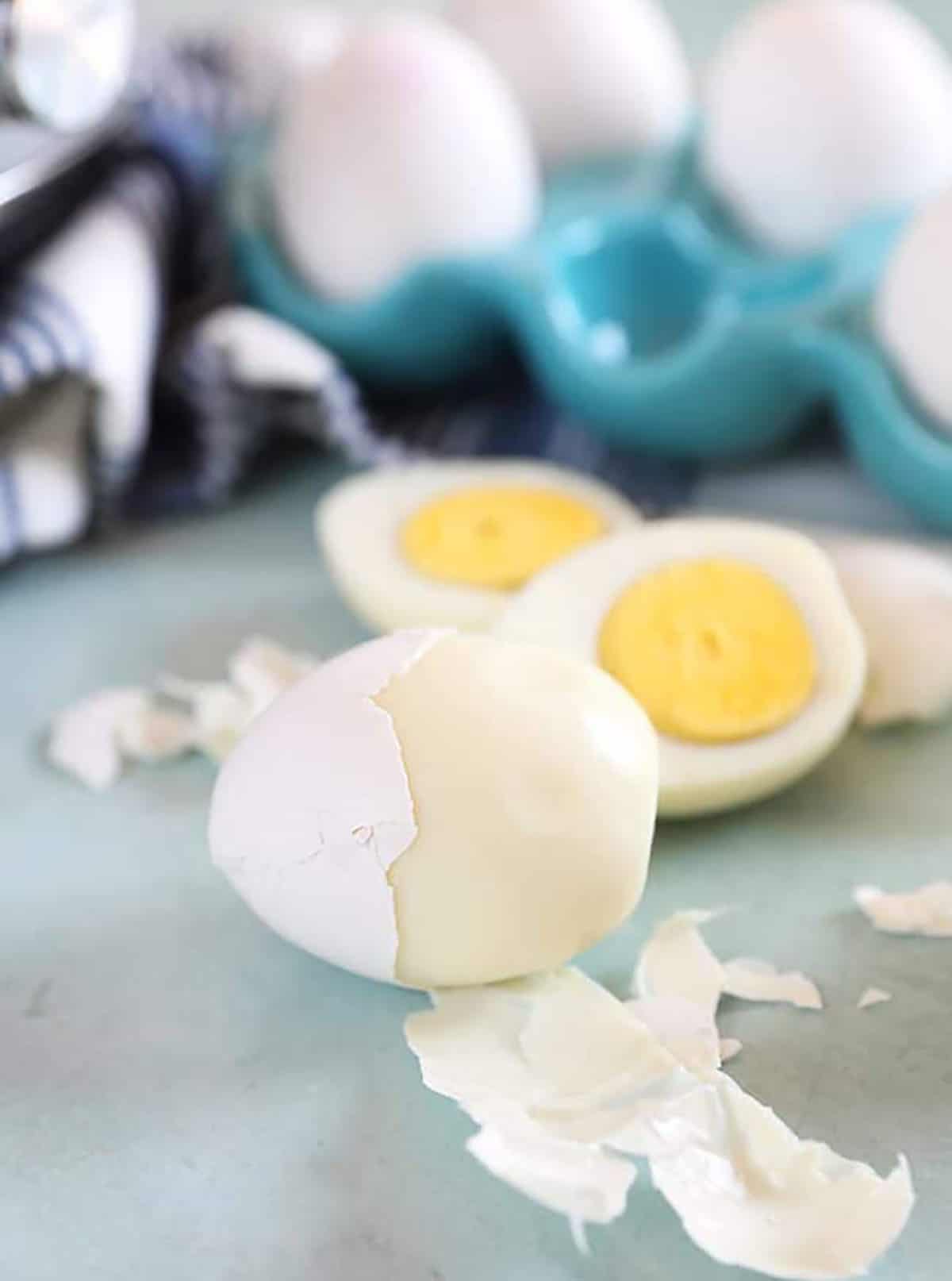 Perfectly peeled hard boiled egg on a blue background with a hard boiled egg cut in half.