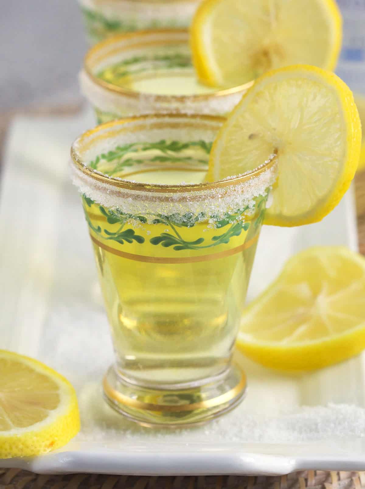 Several shot glasses are garnished with lemon slices and a sugar rim.