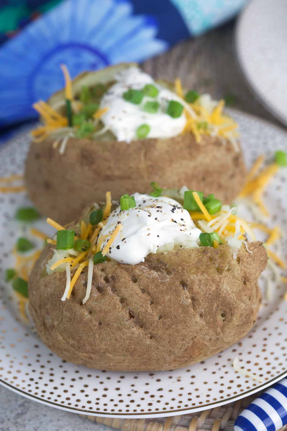 Two baked potatoes are placed on a spotted plate.