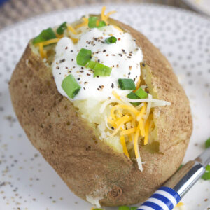 A striped fork is placed next to a cooked and garnished baked potato on a plate.