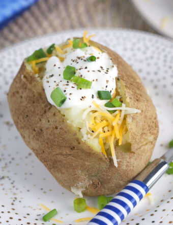 A striped fork is placed next to a cooked and garnished baked potato on a plate.