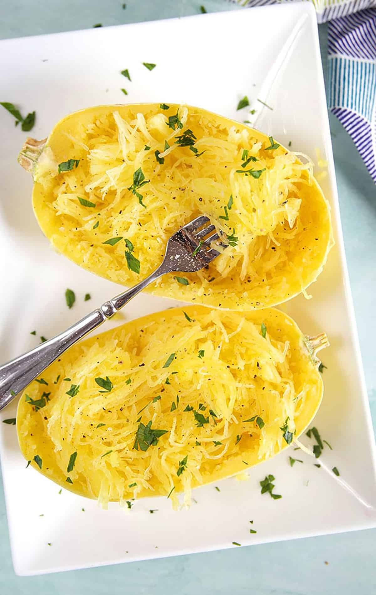 Two halves of spaghetti squash cooked on a white platter with a fork.
