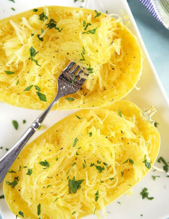 Cooked spaghetti squash with a fork on a white plate.