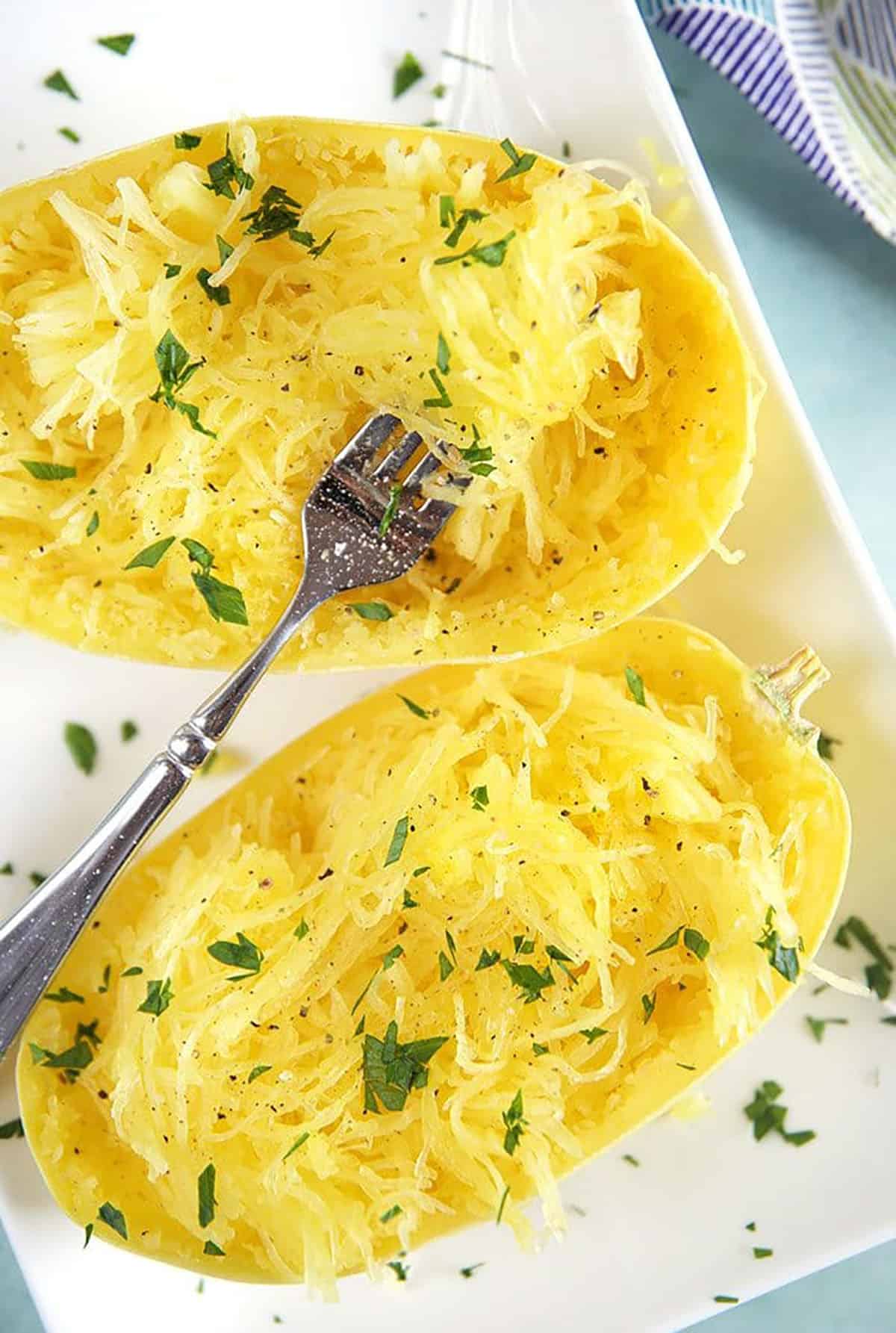 Cooked spaghetti squash with a fork on a white plate.