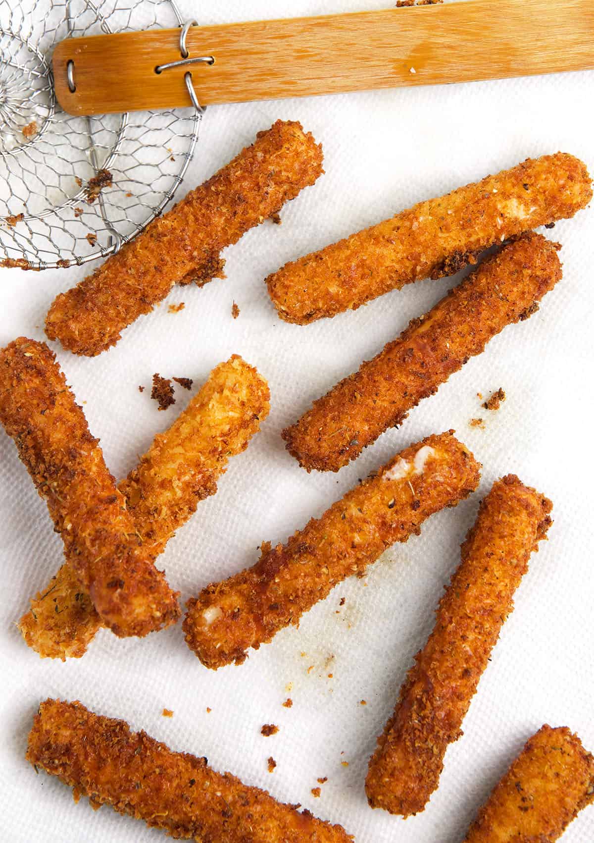 A batch of mozzarella sticks are spread out on a white surface.