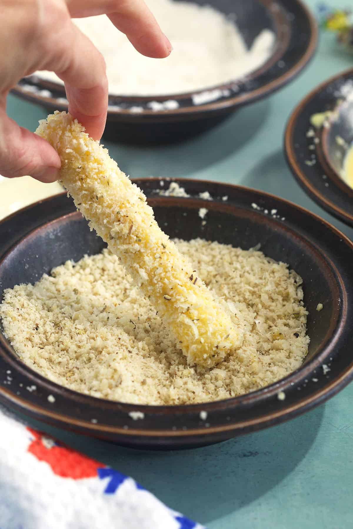 A mozzarella stick is being coated in breadcrumbs.
