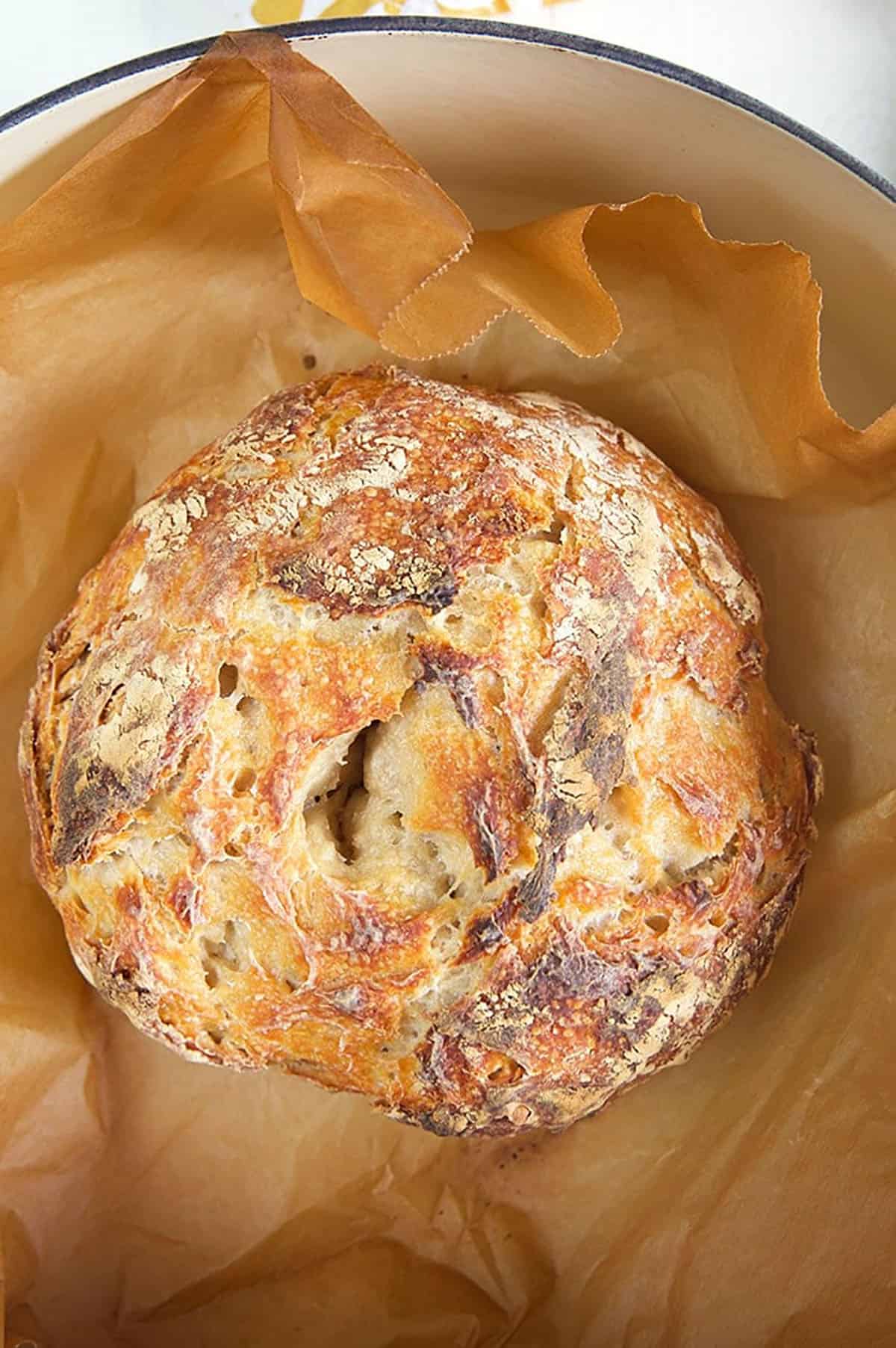Sourdough bread on brown parchment in a dutch oven.