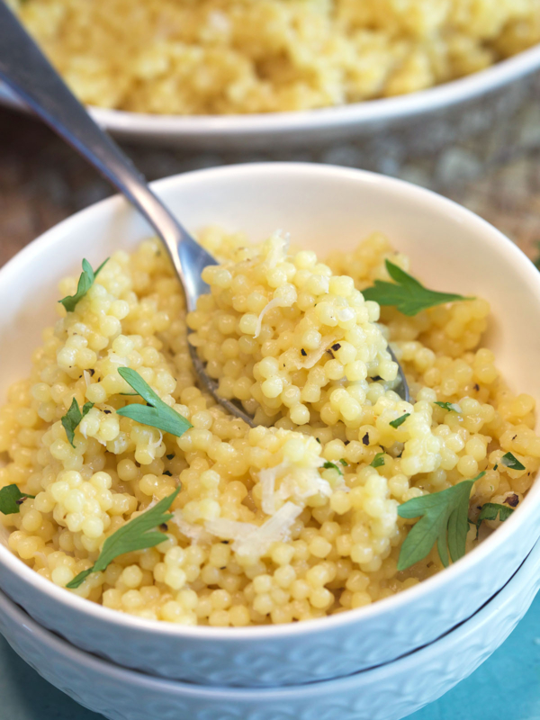 A spoon is lifting a bite sized portion of pastina from the bowl.