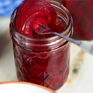 A jar of pickled beets is open with a fork placed on the rim.