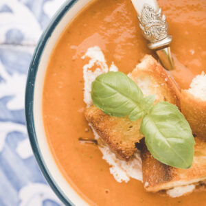 A bowl of roasted tomato soup is topped with basil and croutons.