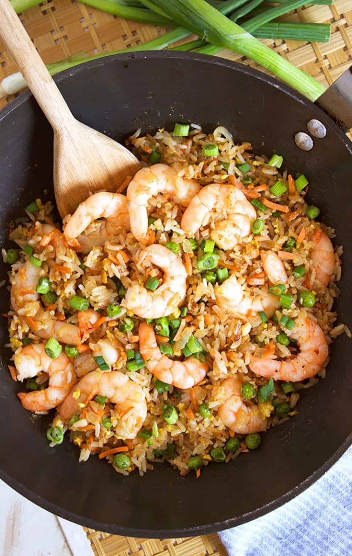 Shrimp fried rice in a wok with a wooden rice paddle.