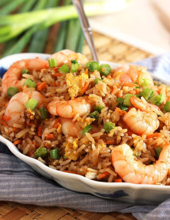 Shrimp fried rice in a serving bowl with a spoon in the background placed on a rattan place mat.