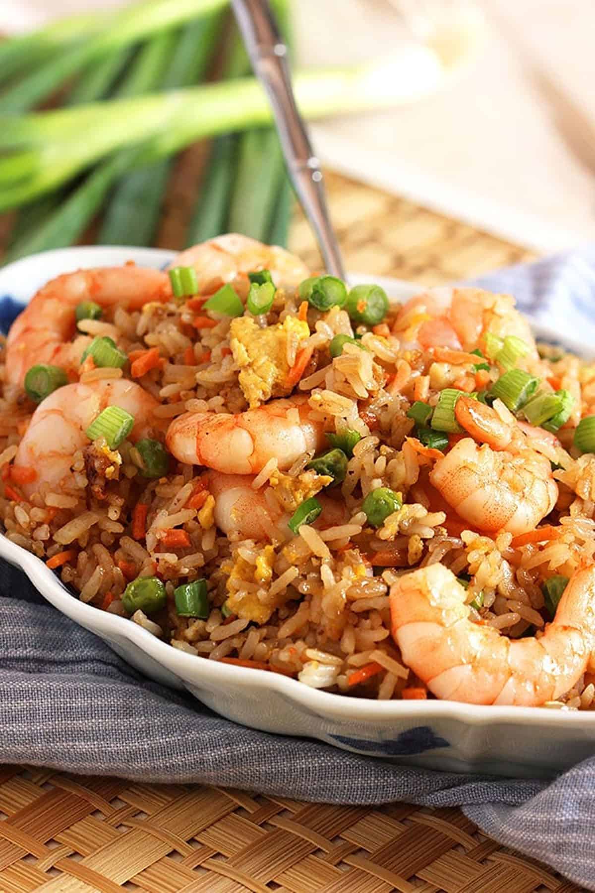 Shrimp fried rice in a serving bowl with a spoon in the background placed on a rattan place mat.