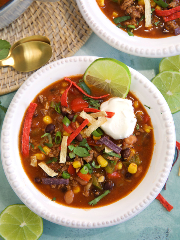 A bowl of taco soup is garnished with a lime slice, sour cream, and tortilla strips.
