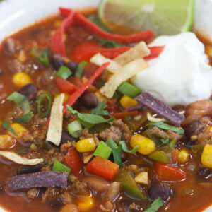 A full, garnished bowl of taco soup is presented in a white bowl.
