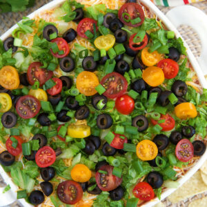 A white square casserole dish is filled with garnished 7 layer dip.