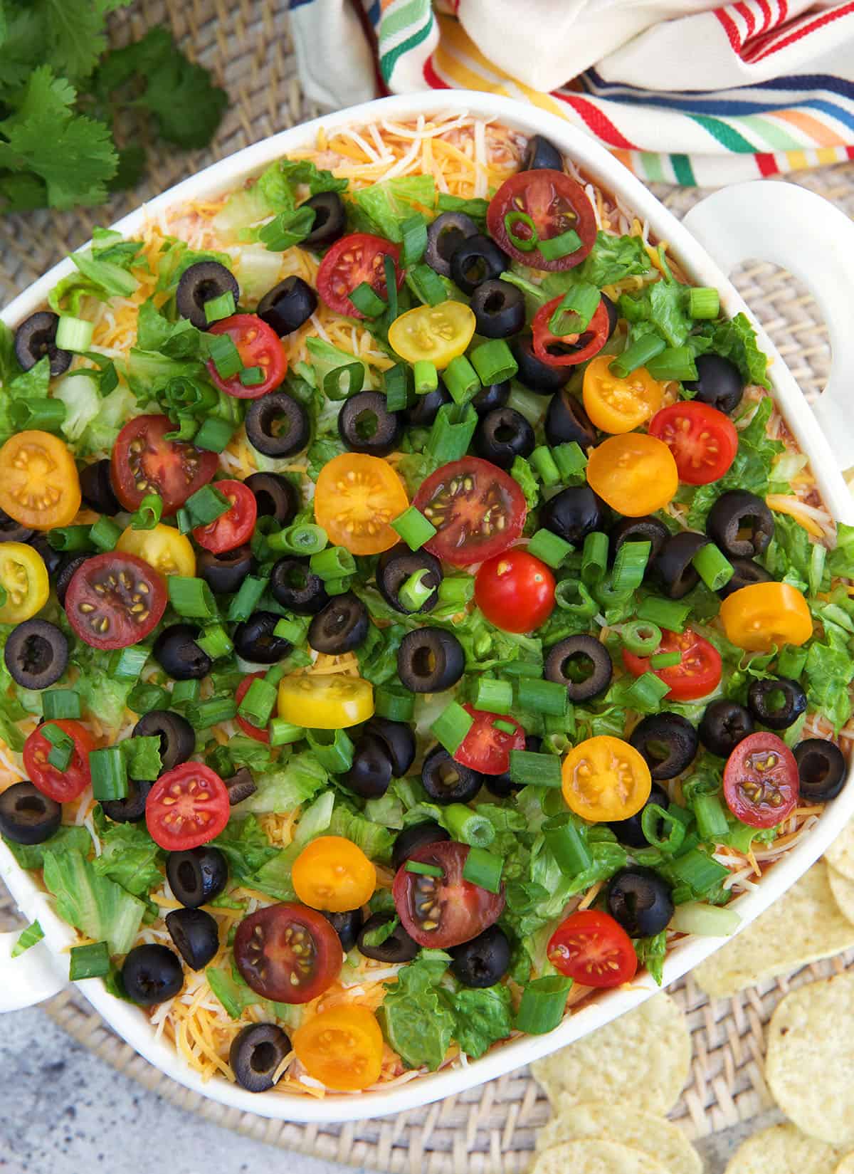 A white square casserole dish is filled with garnished 7 layer dip.
