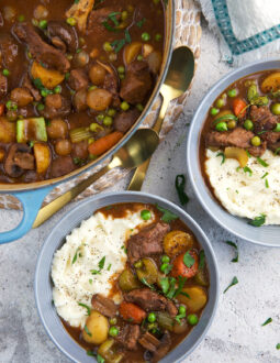 Two full bowls of mashed potatoes and stew are placed next to a full dutch oven.