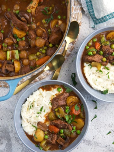 Two full bowls of mashed potatoes and stew are placed next to a full dutch oven.