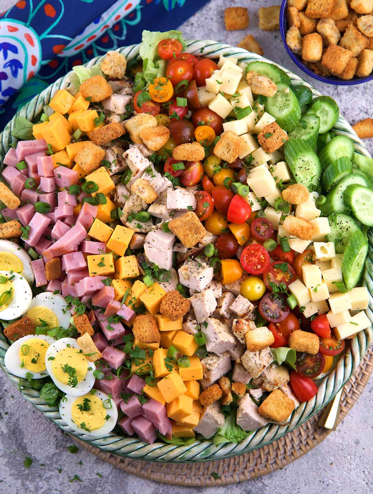A large bowl filled with chefs salad is placed on a tabletop. 