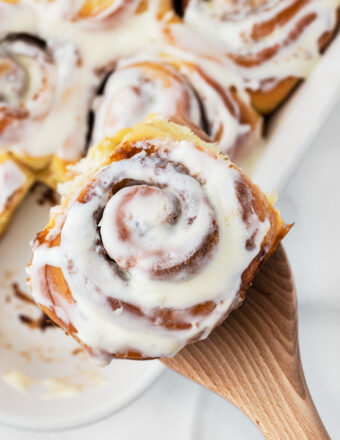 A single cinnamon roll is being lifted by a wooden spoon.