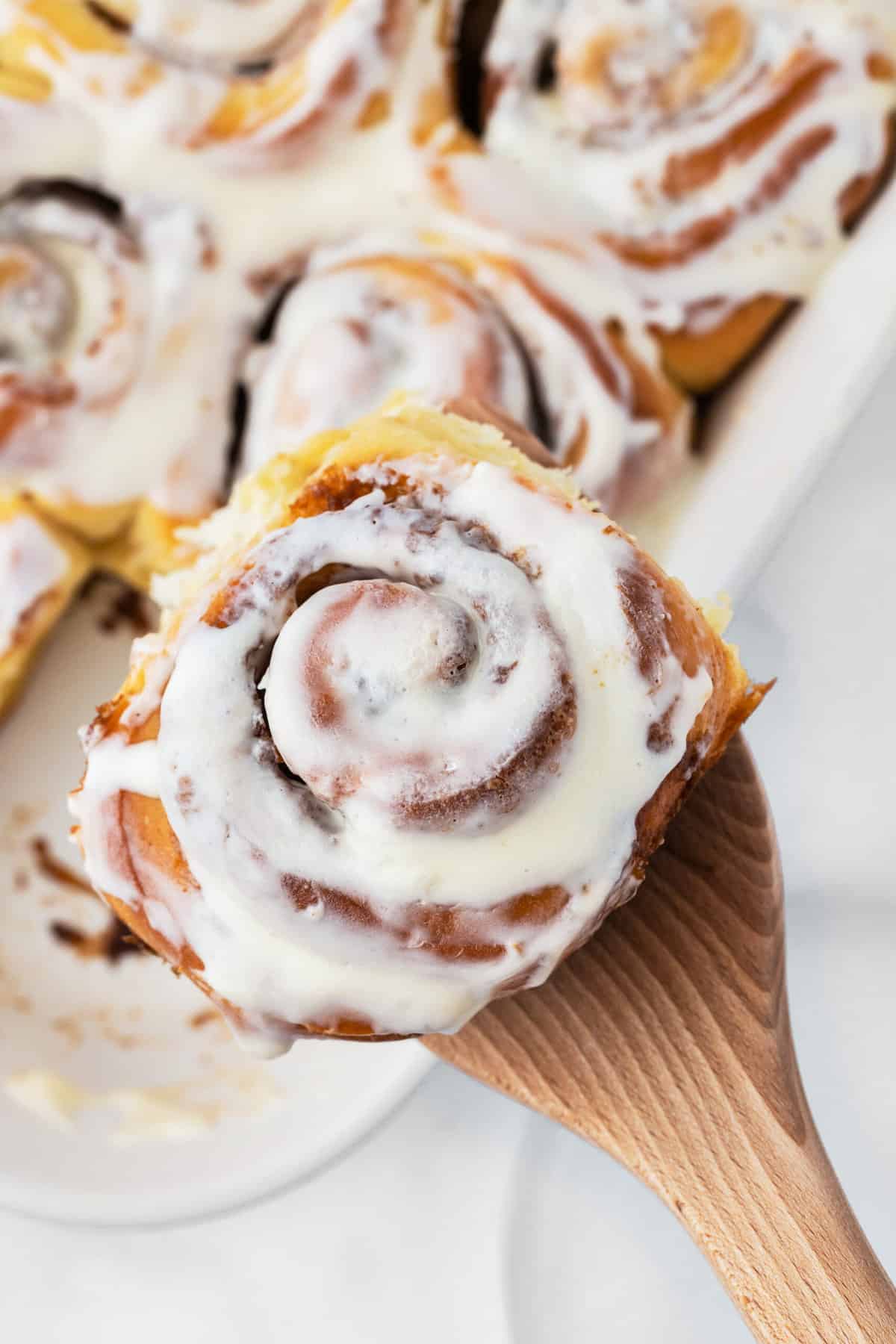 A single cinnamon roll is being lifted by a wooden spoon.