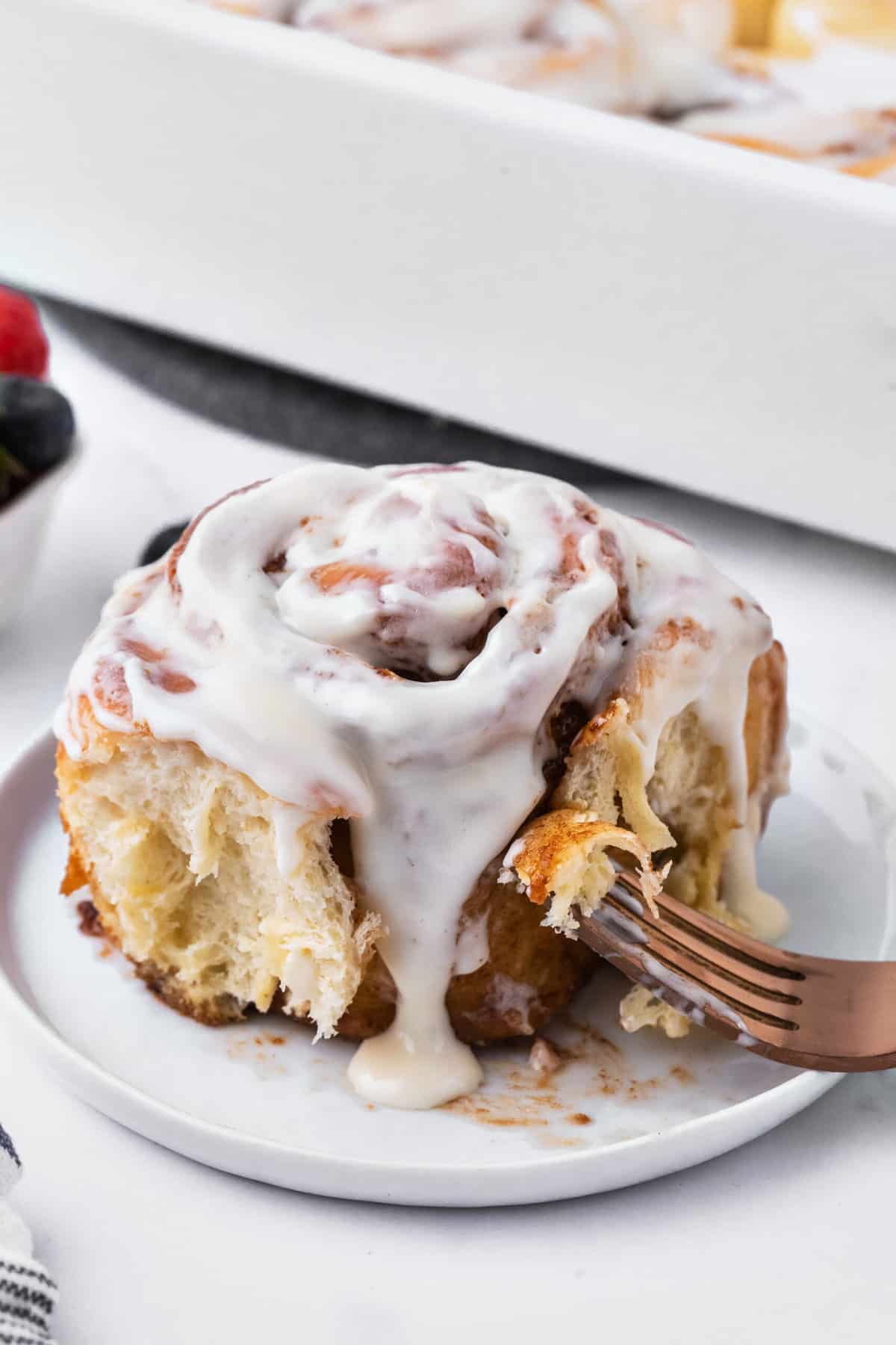 A cinnamon roll is plated with a fork.