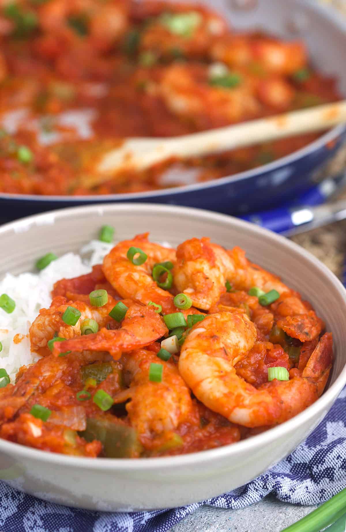 A white bowl is filled with garnished shrimp creole and a serving of white rice. 