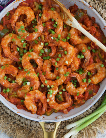 Shrimp are presented in a skillet covered in red sauce and garnished with scallions.