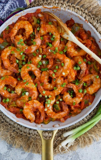 Shrimp are presented in a skillet covered in red sauce and garnished with scallions.