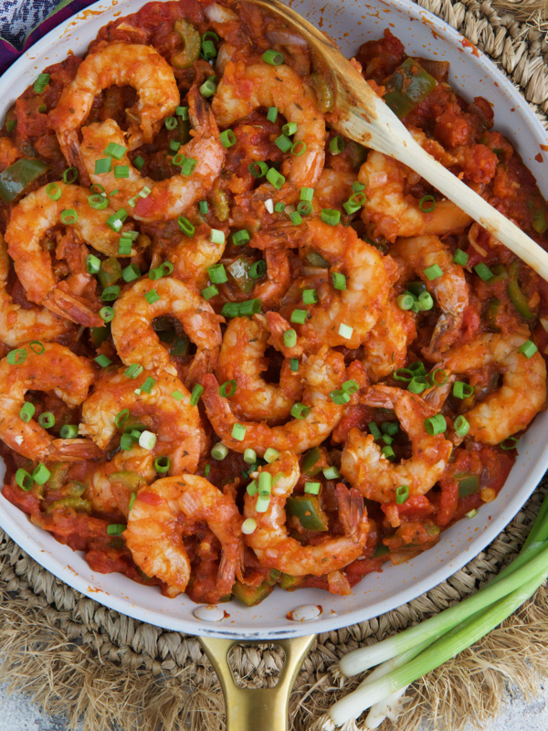 Shrimp are presented in a skillet covered in red sauce and garnished with scallions.