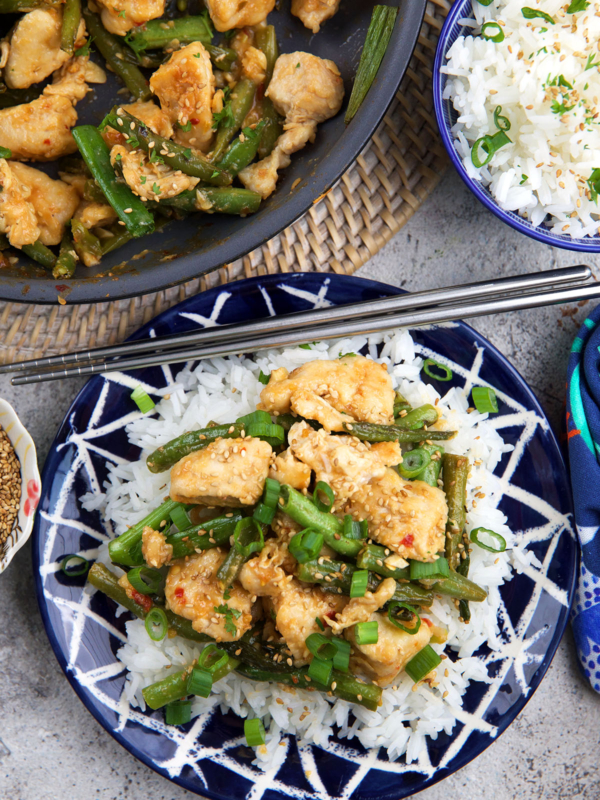 A plate is topped with white rice and hunan chicken is also plated with chopsticks.