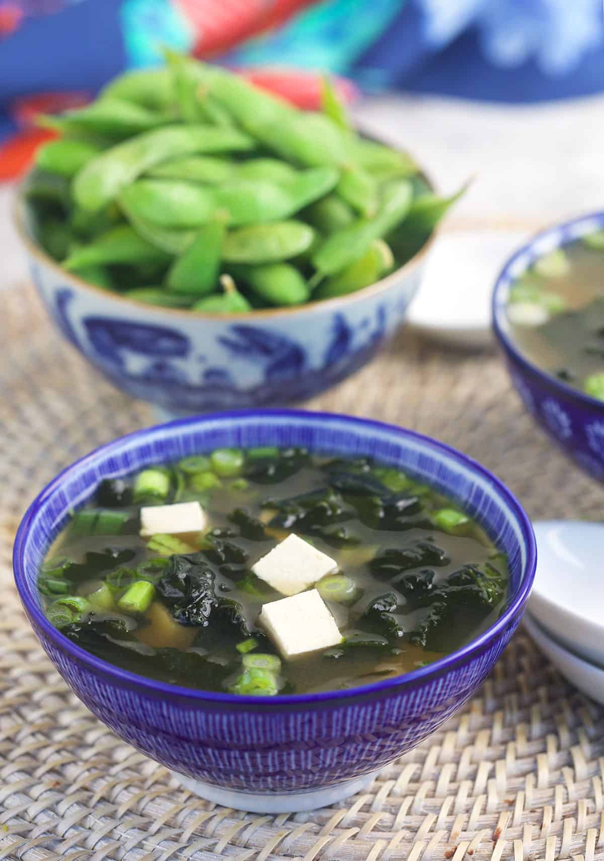 A bowl of edamame is placed next to a bowl of miso soup.