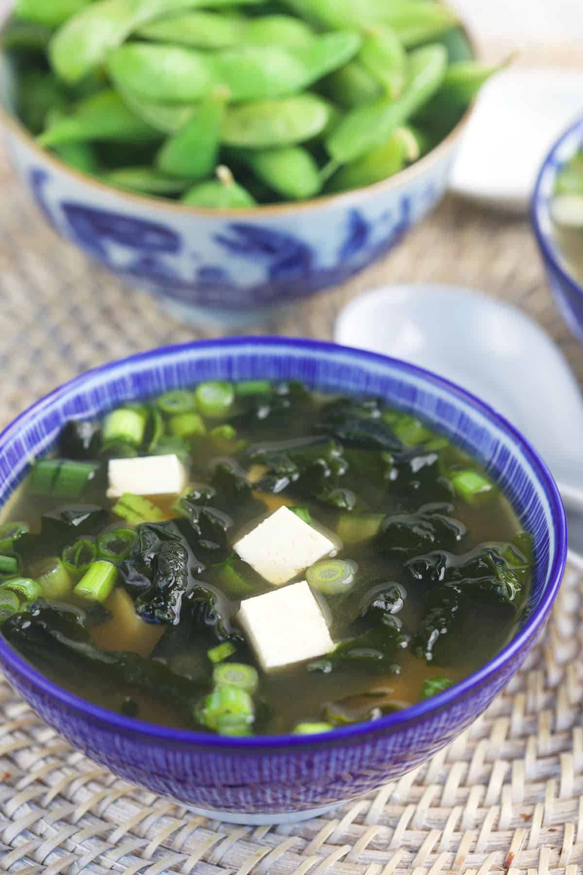 A serving of miso soup is presented in a blue bowl. 
