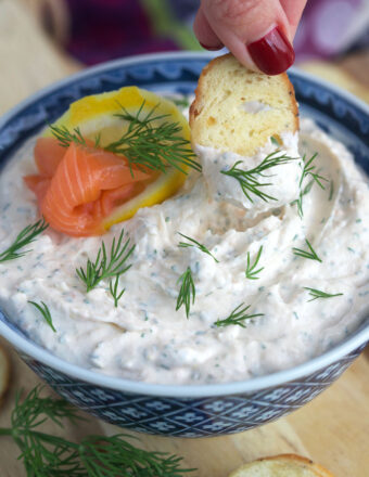 A piece of crostini is being dipped into smoked salmon dip.