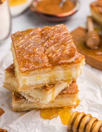 A stack of cheesecake bars are placed next to a honey wand.