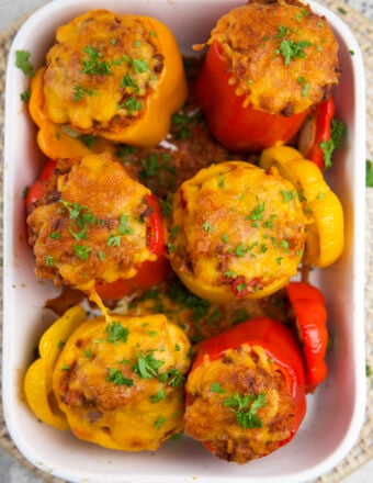 Six baked stuffed peppers are placed in a casserole dish.