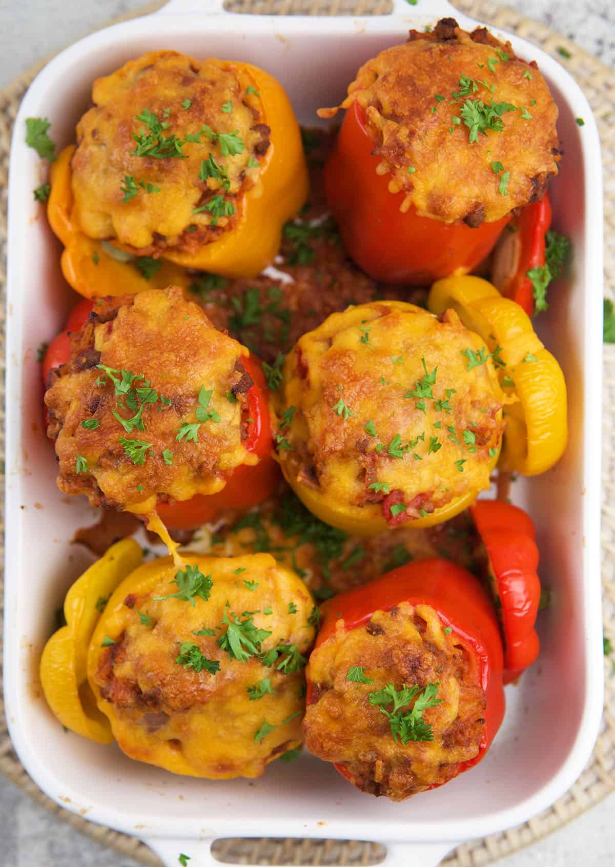 Six baked stuffed peppers are placed in a casserole dish. 