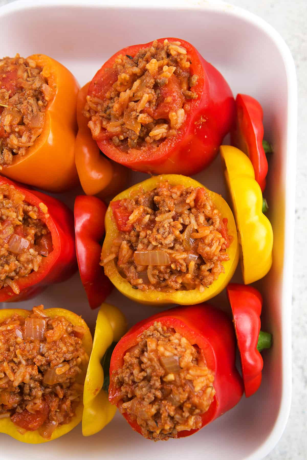 Several stuffed peppers are placed in a large white casserole dish. 